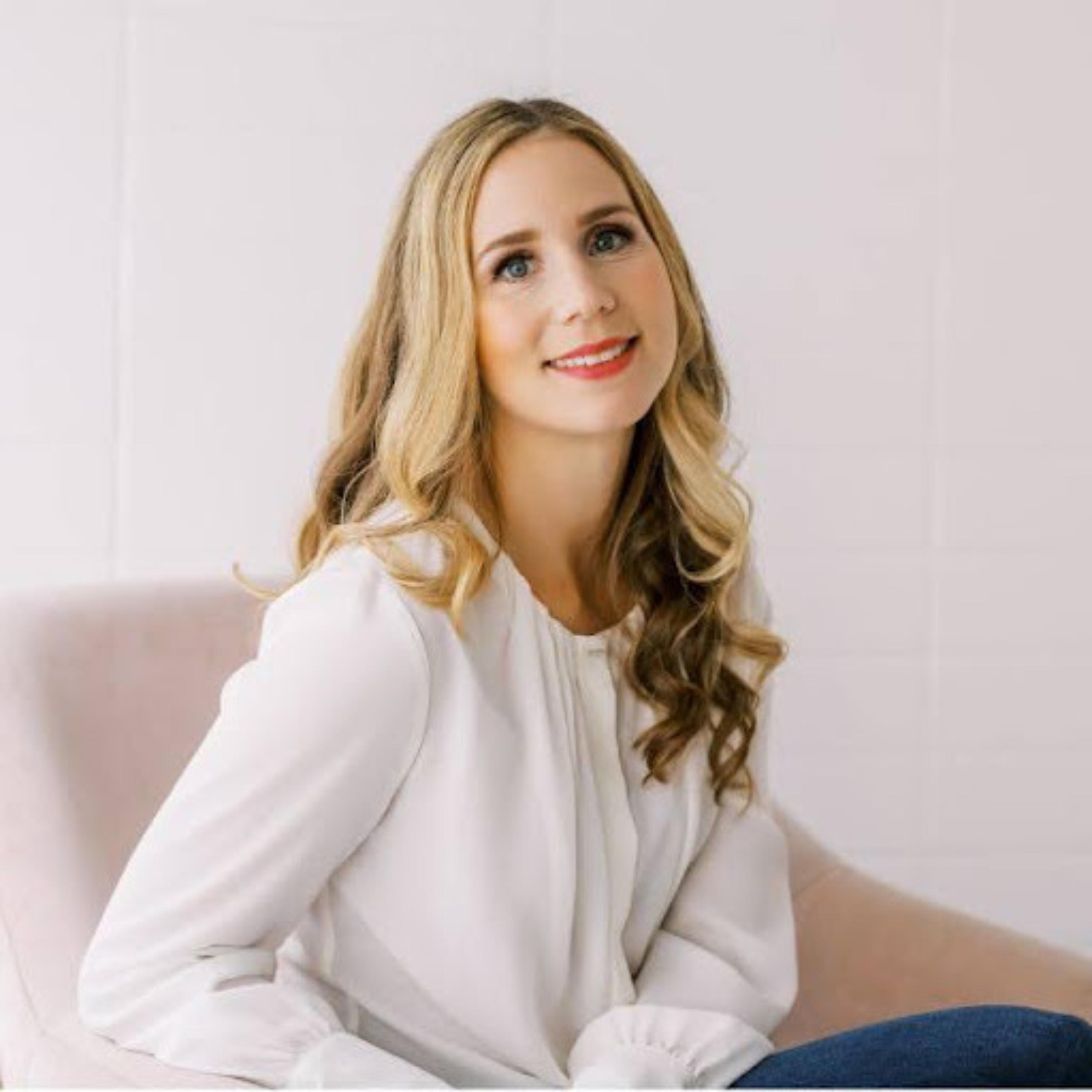 Smiling woman with long wavy blonde hair looking upward from a soft pink chair against a warm peach background.