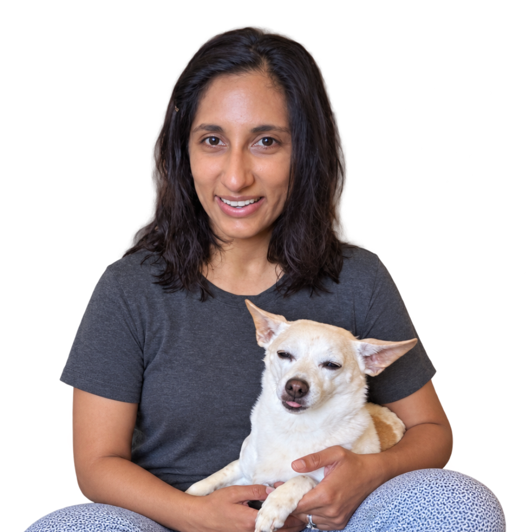 Jaya smiling while holding a small cream-colored dog against a white background.